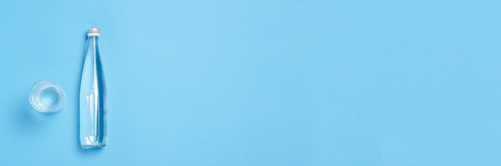 Glass bottle and glass with clear water on a blue background. Concept of health and beauty, water balance, thirst, heat, summer. Flat lay, top view. Banner