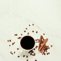 Cup with coffee, cinnamon sticks and coffee beans on a marble background. Flat lay, top view