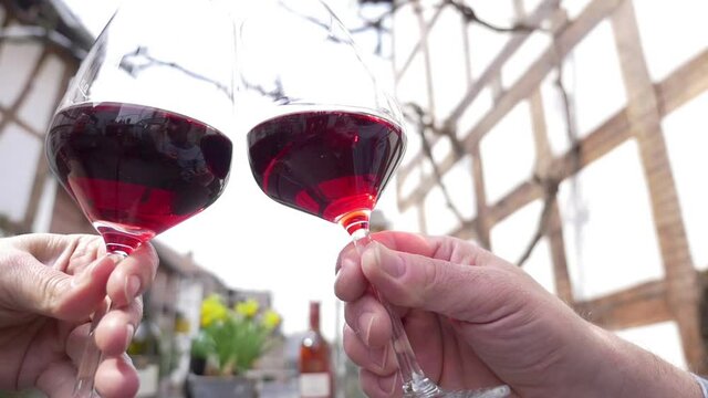 In the timbered house courtyard of an old german winery a man&rsquo;s and a woman&rsquo;s hand clinking two glasses with red wine. Location shot with natural sound and selective focus. 