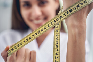 Smiling young woman holding yellow measuring tape