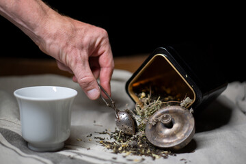 A teaspoon in hand, a box of tea, a white Cup of tea, and scattered tea on the tablecloth