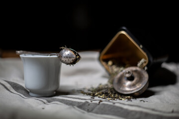 Obraz na płótnie Canvas A teaspoon, a box of tea, a white Cup of tea, and scattered tea on the tablecloth