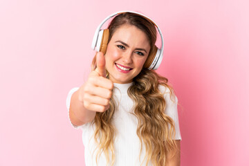 Young brazilian woman isolated on pink background listening music and with thumb up