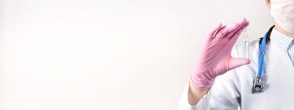 Cropped View Of Young Female Doctor In A White Coat, In A Medical Mask And Pink Sterile Gloves Holding Ampoule Vaccines For Children Or Older Adults. Concept: Diseases, Medical Care, Science