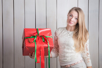 attractive slim blonde girl looks at camera holding in hands big red gift box