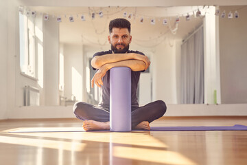 Bearded man with foam roller sitting on the floor in yoga studio