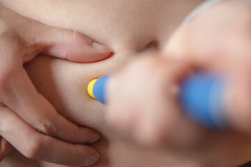 Woman using a pre-filled syringe or pen injection into the abdominal area, closeup