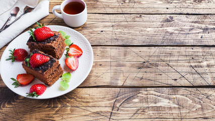 Chocolate truffle cake with strawberries and mint. Wooden table. Copy space