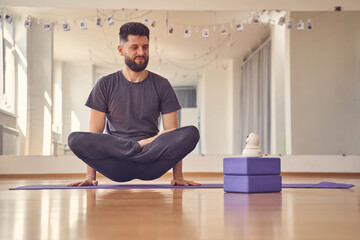 Handsome young man doing lifted lotus or scale pose