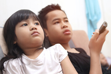 Young Asian boy and girl sibling sitting on the couch and watching tv