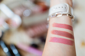 Female hand holding lipsticks and color swatches painted on hand.