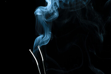White puffed smoke coming out of sticks in a dark background