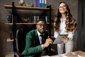 Young modern man and pretty girl in business clothes working using a tablet in a creative office