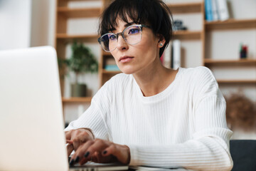 Photo of serious woman working with laptop while sitting at table