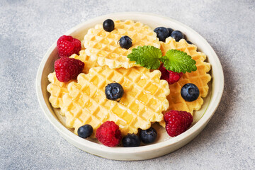 Corrugated waffle cookies with fresh raspberries and blueberries on a concrete background. Copy space.