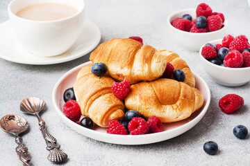 Croissants with fresh raspberries and blueberries on grey concrete background. Copy space. concept of Breakfast coffee honey