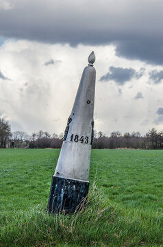 Dramatic sky over a boundery marker with inscription 1843 in a meadow on the otherwise hardly noticable border between the Netherlands and Belgium near Valkenswaard