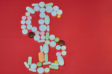 Conceptual background on the commercial theme of pharmacology and the production of medicines and drugs, tablets laid out in the form of a dollar sign on a red background with a sun flare.