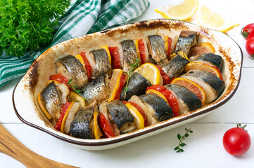Baked fish with vegetables. Pieces of herring, onion, tomato, lemon, aromatic herbs