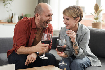 Happy couple sitting on the sofa with wineglasses of wine and laughing they spending funny time together