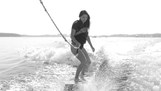 Black and white video of a girl riding a wakeboard on the river. A sportswoman learns to ride a game.