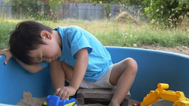 4K Asian child boy playing car truck toy and sand in sandbox with happy face outdoor with rural natural background. Family relax and freedom time in summer holiday.
