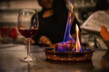 Traditional portuguese sausage chourico aka spanish chorizo sliced and flame-cooked over alcohol in an earthenware dish served with a glass of chilled red port wine, a fado house, Lisbon, Portugal