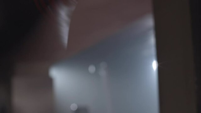 Side view of small punching bag hanging in foggy backlight and unrecognizable boxer fighting it. Sportsman training using equipment in haze. Combat sport, martial arts. Cinema 4k ProRes HQ.