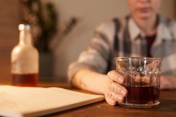 Close-up of young woman sitting at the table and drinking alcohol cocktail at home