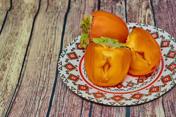 Fresh organic persimmon in vintage plate on rustic wood background. Concept for healthy food, vegan or raw diet.Copy space.