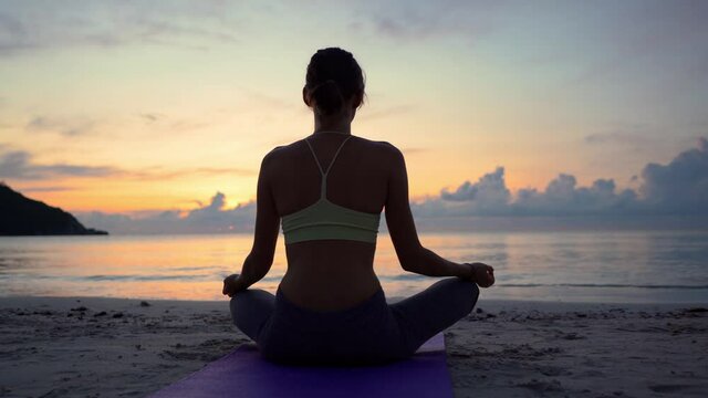 Yoga meditation, woman meditating at beach sunset or sunrise relaxing in yoga pose. Serene relaxed female yoga in calm nature sea scene.