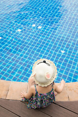Selective focus and above shot with copy space of adorable 4-year-old asian girl sitting beside the pool with blue and clear water with fun and happiness during the summer vacation with the family.