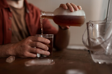 Close-up of man sitting at the table and pouring wine from the bottle in his glass he has problems with alcohol