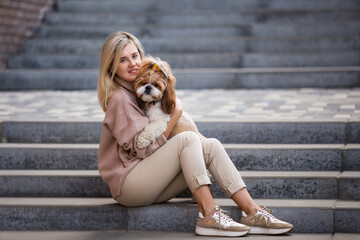 Beautiful woman hugs her favorite dog Shih Tzu. Sitting in a stone staircase. Lifestyle