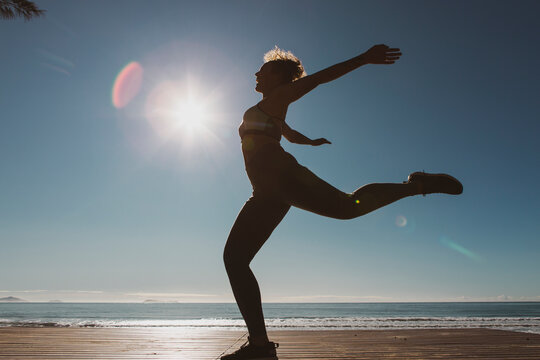 Young female dancer dances at sunset wearing sportswear . Silhouette backlight of the sun with body movements. Freedom and happiness concept.