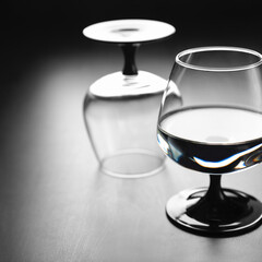 Two glasses on a black leg, one with water, the second turned upside down, against a dark...