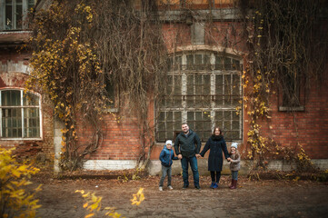 Obraz premium A wonderful sweet family stands near an old brick house in the fall, they hold hands and smile. Soft focus.