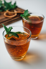 Golden drink, iced tea with a ring of dried orange and mint on a white background.