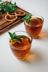 Golden drink, iced tea with a ring of dried orange and mint on a white background.