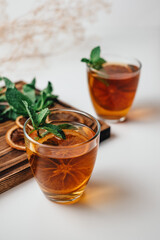 Golden drink, iced tea with a ring of dried orange and mint on a white background.