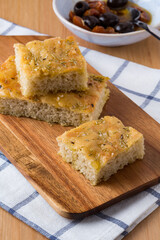 Focaccia and olives on a wood board and a fabric tissue
