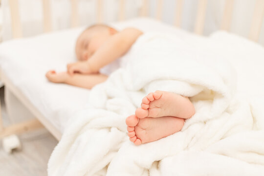 baby's legs in focus against the background of a sleeping baby in a white bed, a healthy and calm baby's sleep