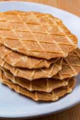 A pile of waffles biscuits on a white plate dish on a wood table