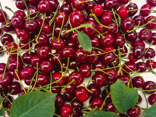 Juicy ripe red cherries with green leaves scattered on a light background.