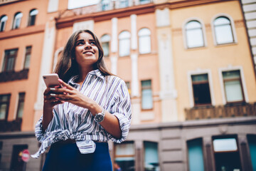 Below view of dreamy young woman with blonde hair thinking on creating own blog with interesting trips standing outdoors in modern downtown near publicity area for your advertising text message