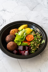 Healthy Vegan Take Away Falafel Bowl with Mung Bean Salad, Legume, Roasted Beet and Yellow Turmeric Hummus Tahini Sauce in Black Plastic Plate Cup Package / Container.
