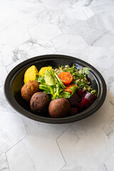 Healthy Vegan Take Away Falafel Bowl with Mung Bean Salad, Legume, Roasted Beet and Yellow Turmeric Hummus Tahini Sauce in Black Plastic Plate Cup Package / Container.