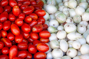 Grape tomatoes and white onions lie side by side at an outdoor produce market.