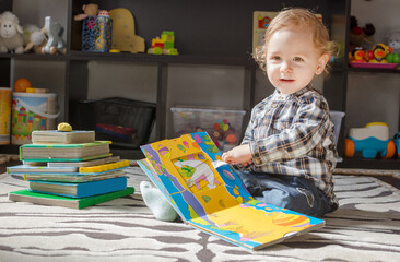 Fototapeta premium Happy sweet child reading books sitting on the floor, at home
