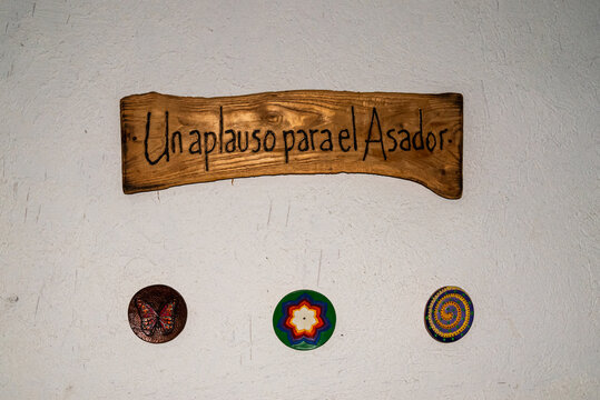 a painted `Un aplauso para el Asador&acute; wooden signboard on aged white texturized wall